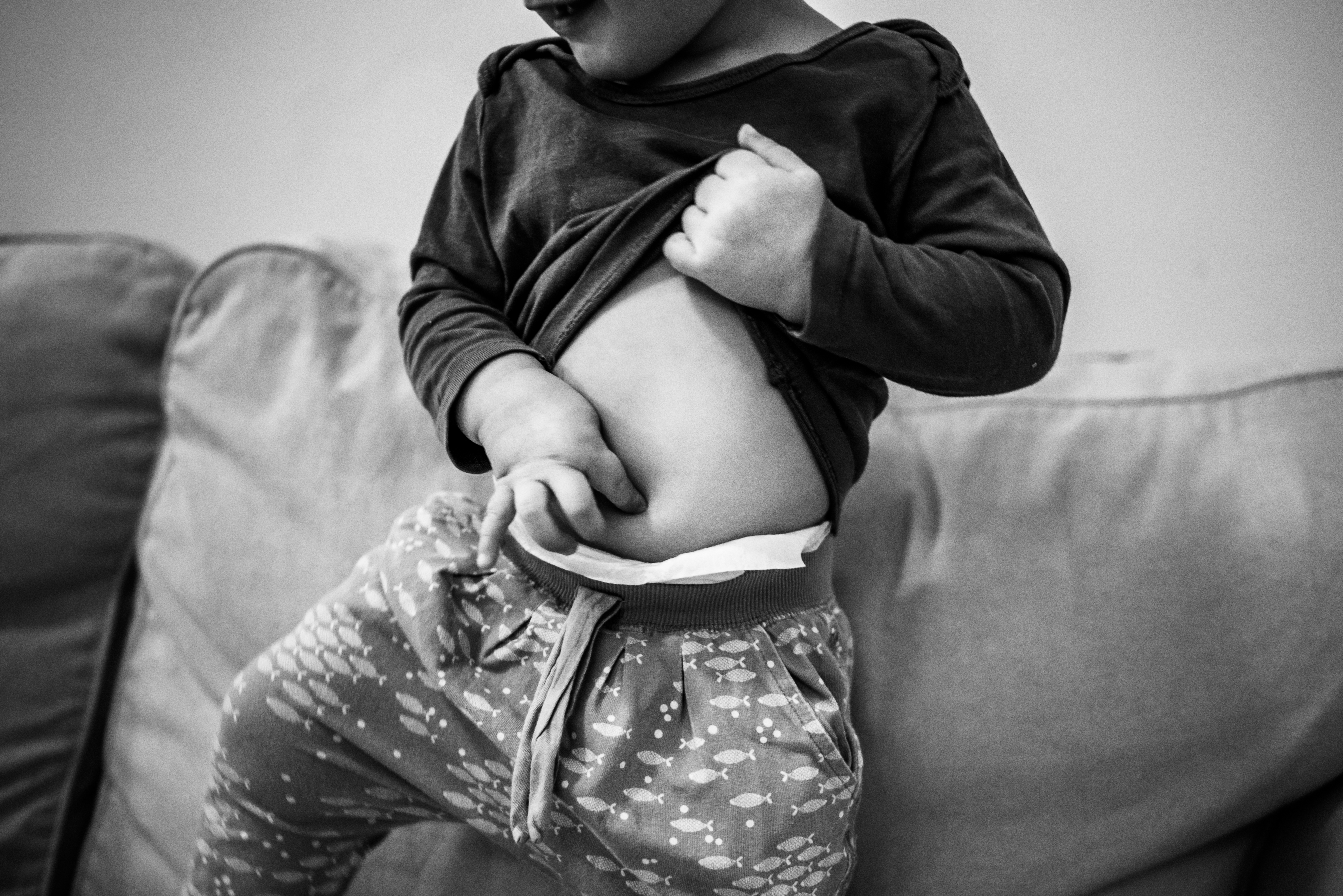 małe dziecko sprawdza, czy ma pępuszek, na zdjęciu widać słodki brzuszek z podwinięta koszulką fotografia rodzinna agnieszka mocarska warszawa